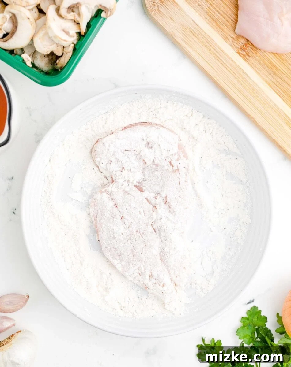 Simple Weeknight Chicken Marsala 5 A piece of chicken breast, thoroughly coated in a light flour mixture, rests in a shallow white bowl.