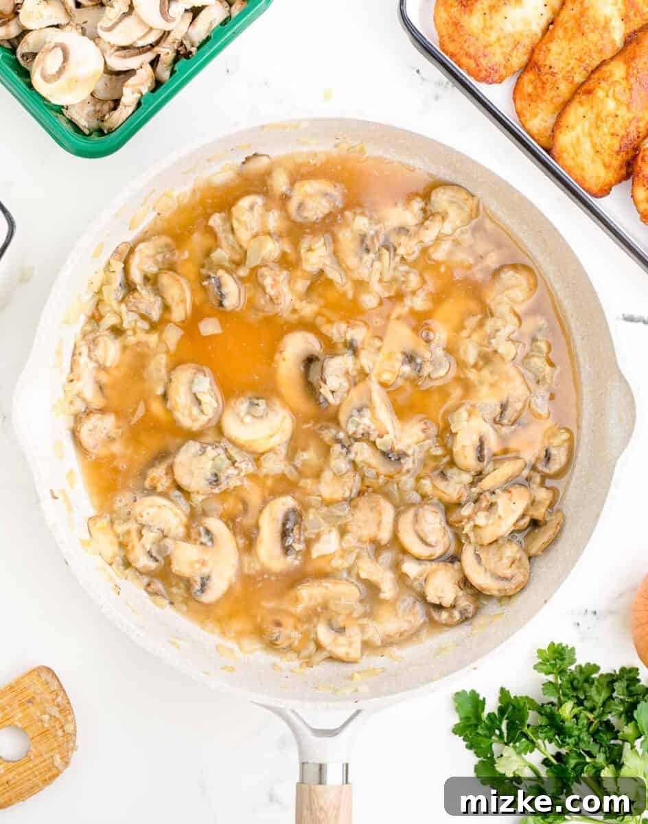 Simple Weeknight Chicken Marsala 8 Fresh sliced mushrooms are being sautéed in a hot white pot, starting to soften and brown.