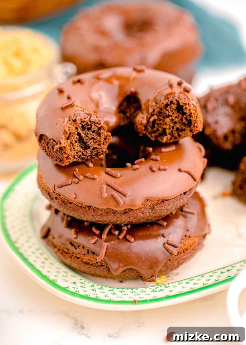A beautifully halved chocolate frosted donut stacked on top of two other whole donuts, showcasing its moist, fluffy interior and generous frosting.