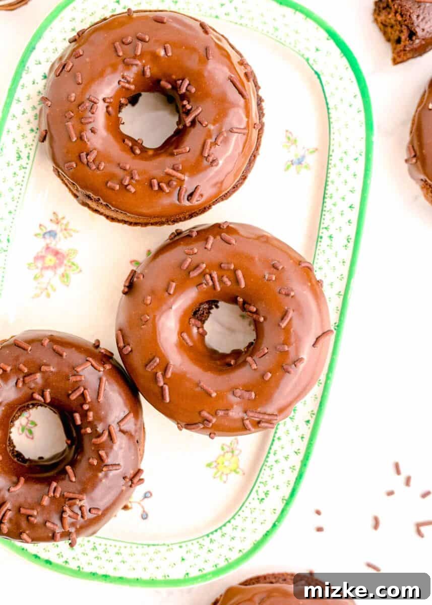 Three perfectly chocolate frosted donuts arranged on a pristine white platter, ready to be enjoyed.