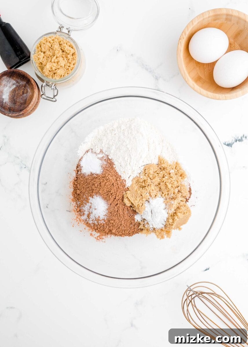Dry ingredients for donut batter, including flour and cocoa, are measured into a large glass mixing bowl.