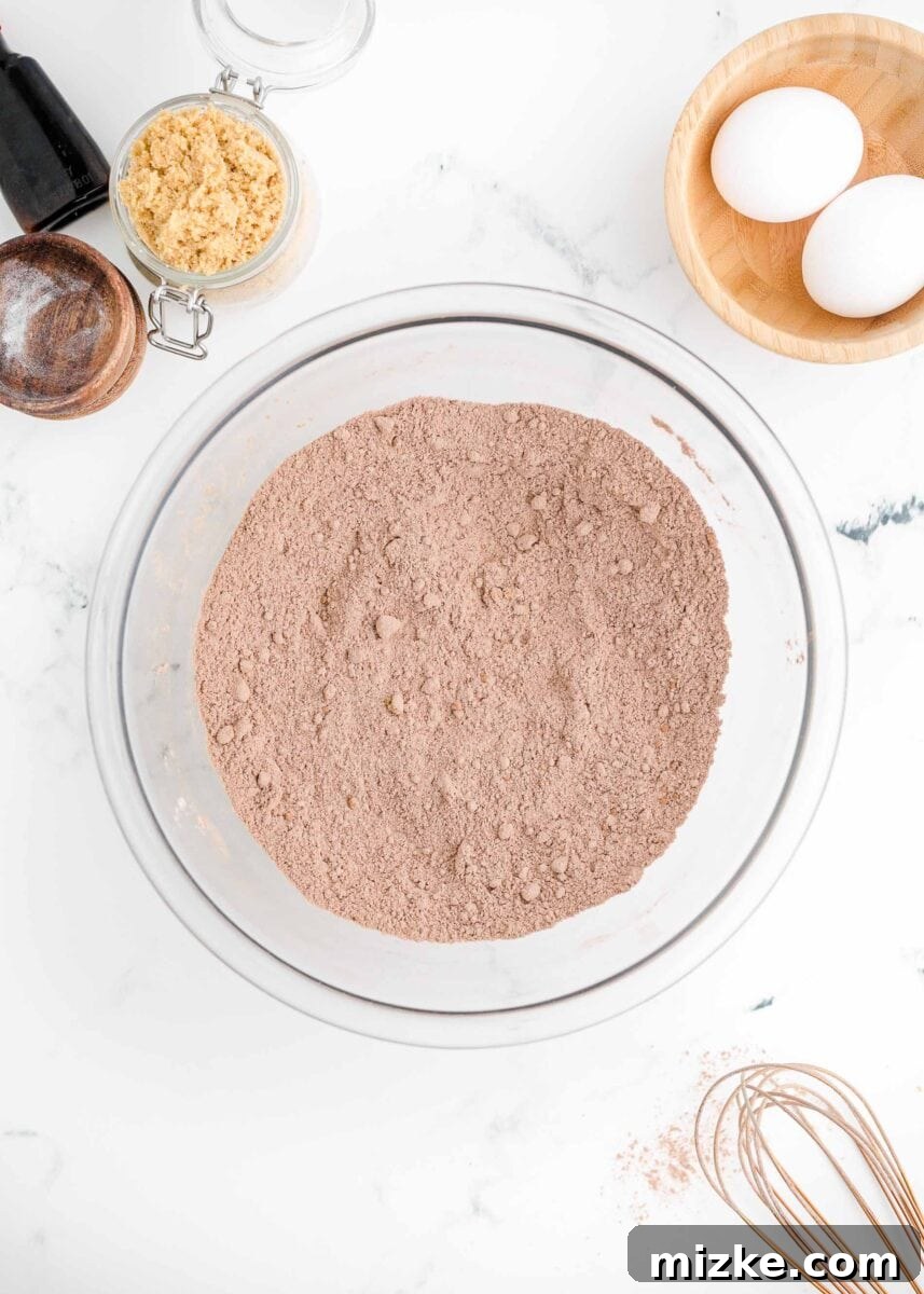 The dry ingredients for the chocolate donut batter are thoroughly whisked together in a glass bowl.