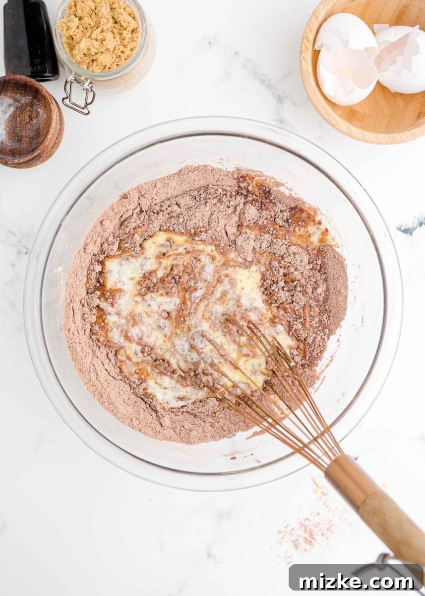 Wet ingredients for donut batter, including eggs, buttermilk, and melted butter, are being whisked until smooth.