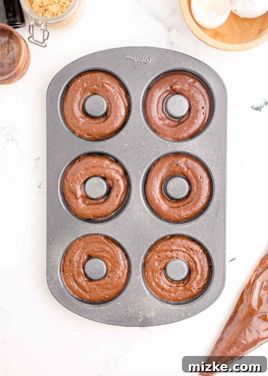 Donut batter neatly piped into a baking tin, each cavity filled about two-thirds full, ready for the oven.