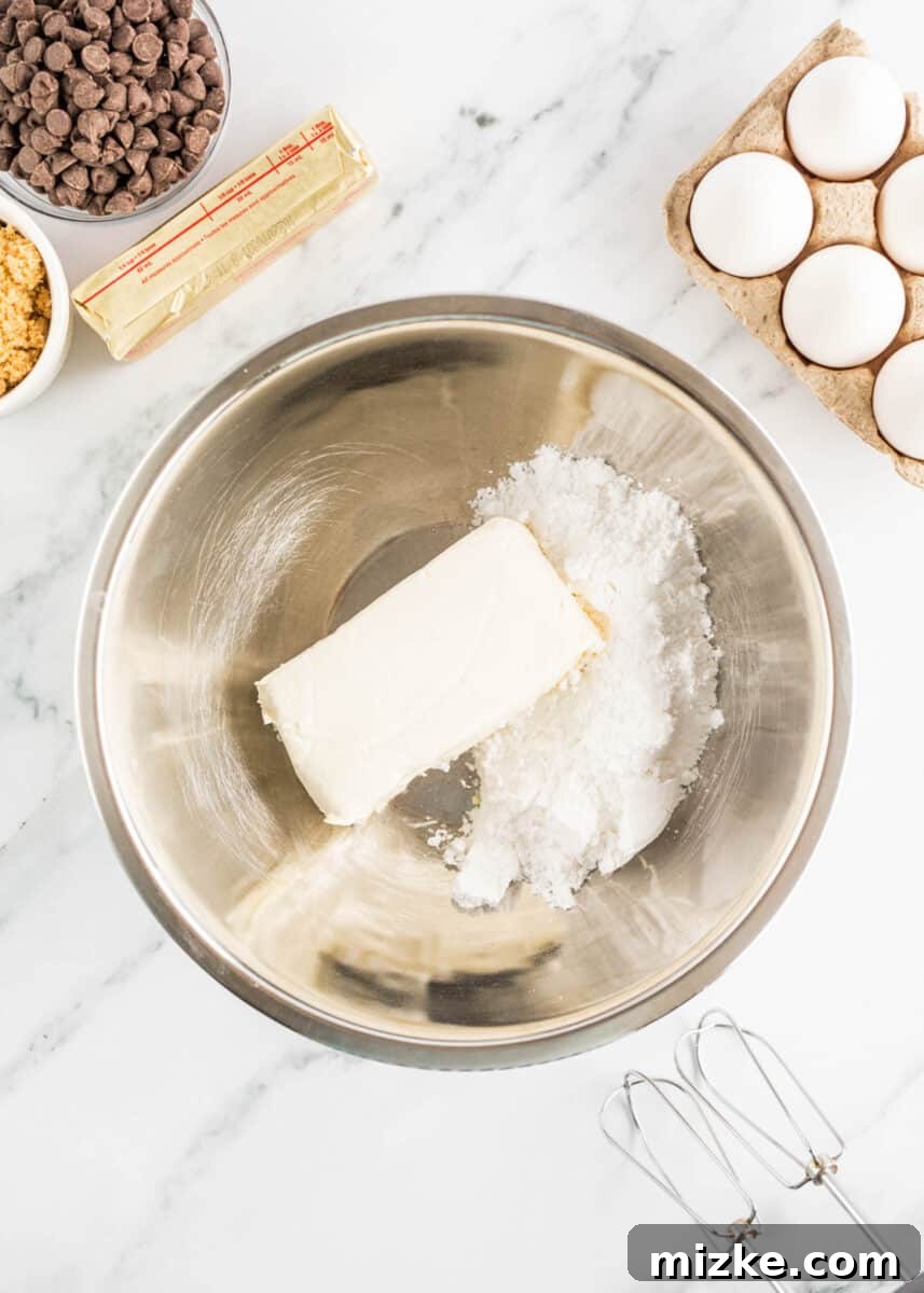 Decadent Cheesecake-Stuffed Chocolate Chip Cookies 4 cream cheese and sugar are both placed in a large bowl, ready to be mixed.