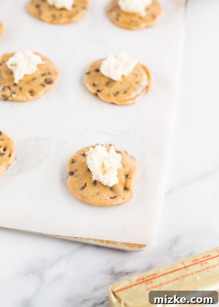 Decadent Cheesecake-Stuffed Chocolate Chip Cookies 8 a cheesecake dollop is placed in the center of raw cookie dough pieces on a baking sheet.