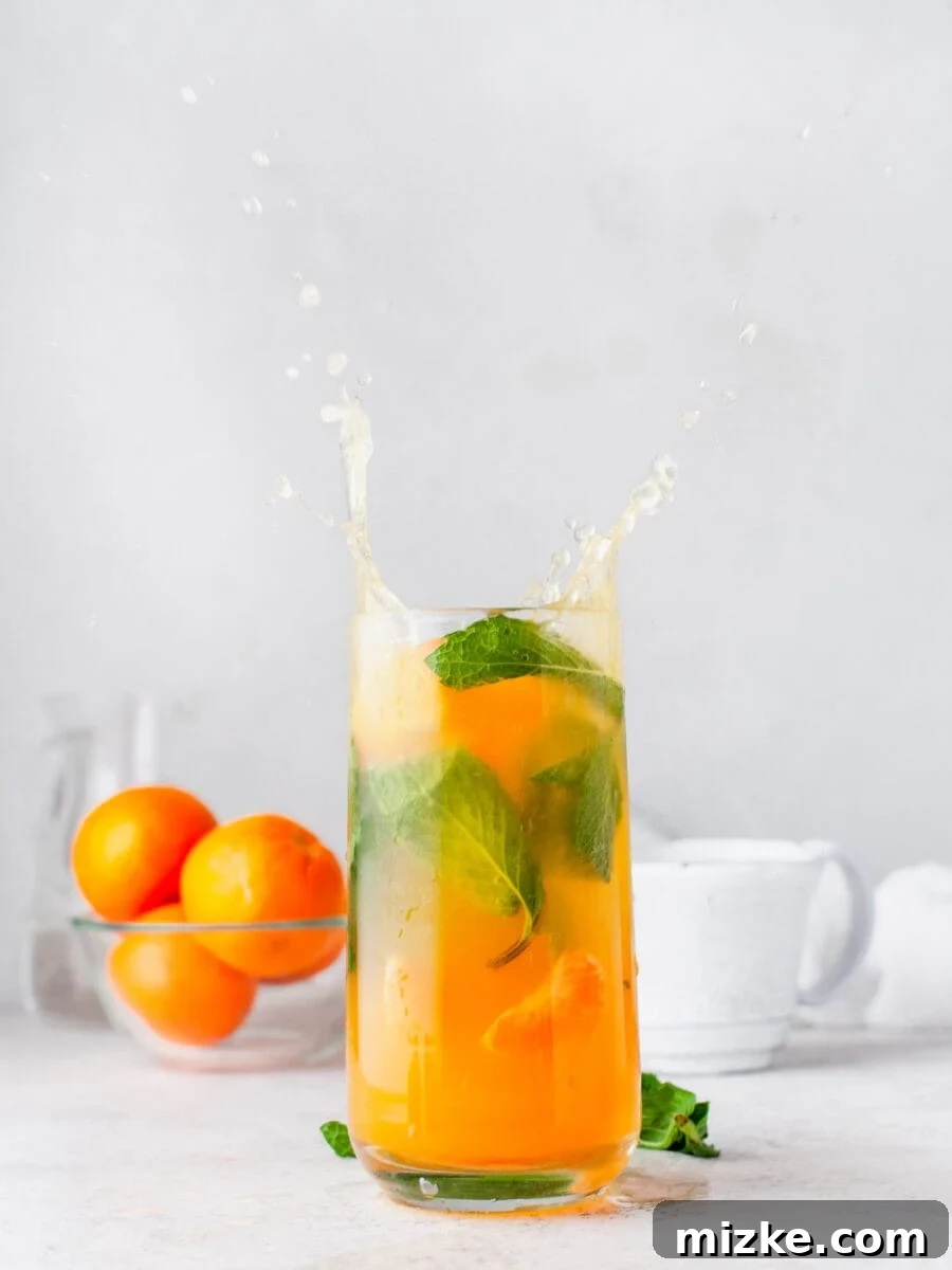 Sun-Kissed Mint Splash 2 A vibrant Orange Mojito splashing in a tall, elegant glass, garnished with fresh mint and orange slices.