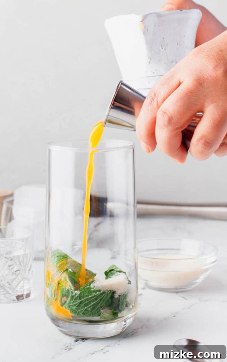 Sun-Kissed Mint Splash 5 Freshly squeezed orange juice is being poured into a glass already containing muddled mint leaves, a key step for an Orange Mojito.