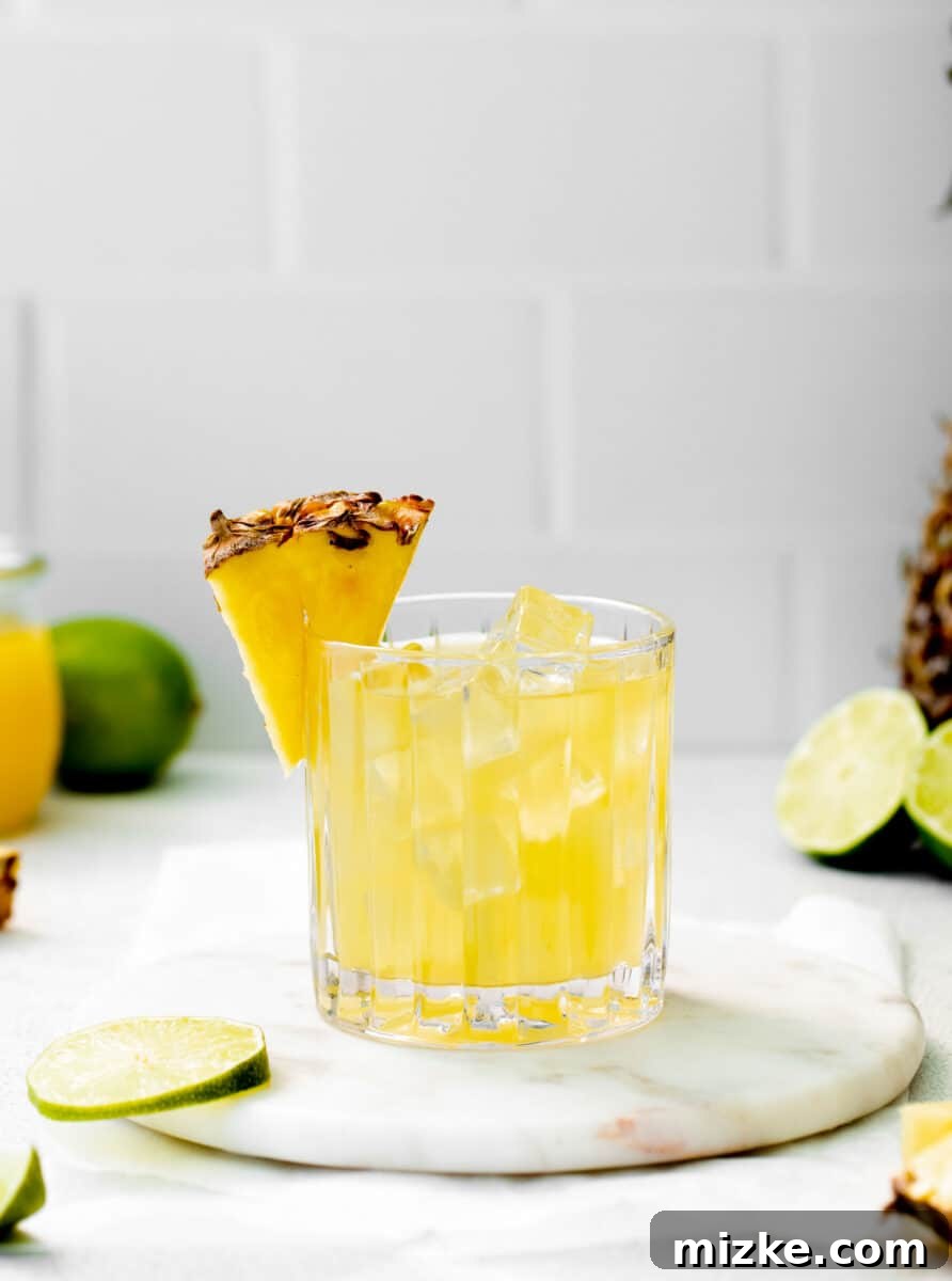 A vibrant Pineapple Paloma glass, elegantly garnished with a fresh pineapple wedge on the rim, beckons for a refreshing summer sip.