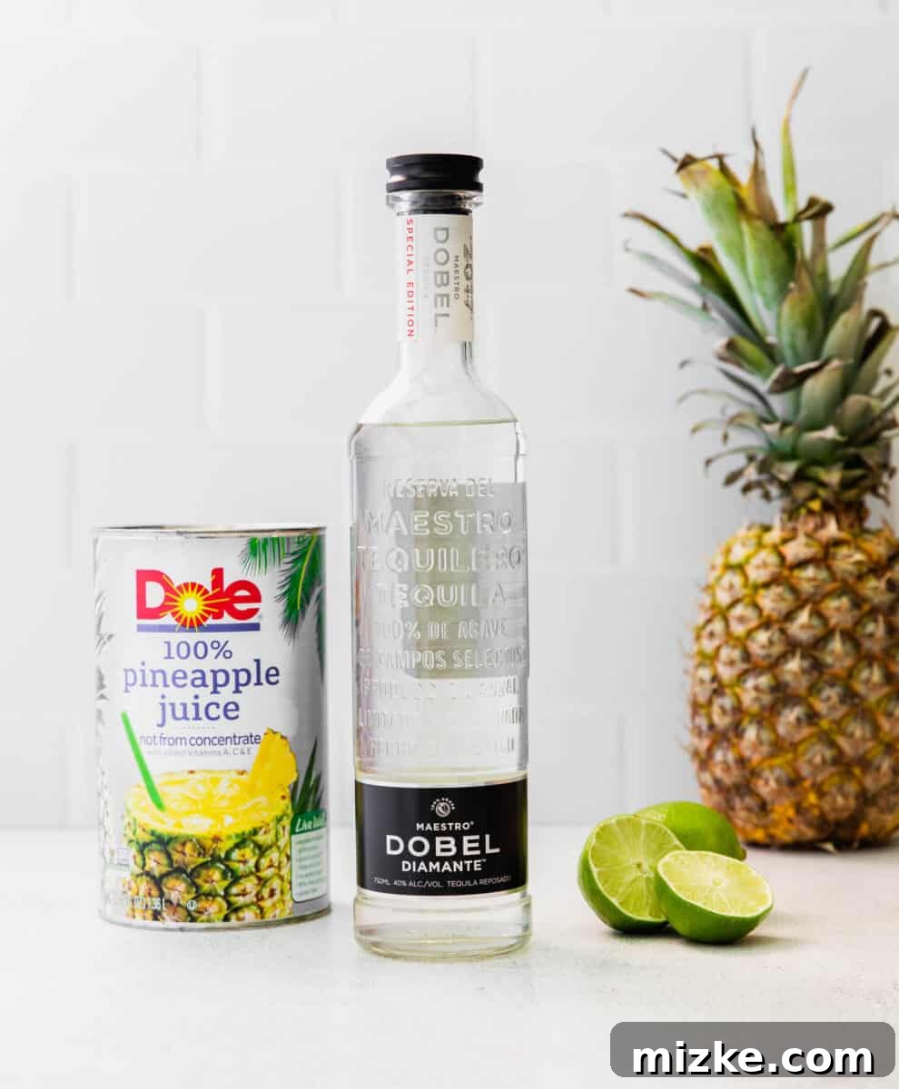 A collection of fresh ingredients for a Pineapple Paloma, including a bottle of tequila, fresh limes, and a carton of pineapple juice, artfully arranged on a pristine white countertop.