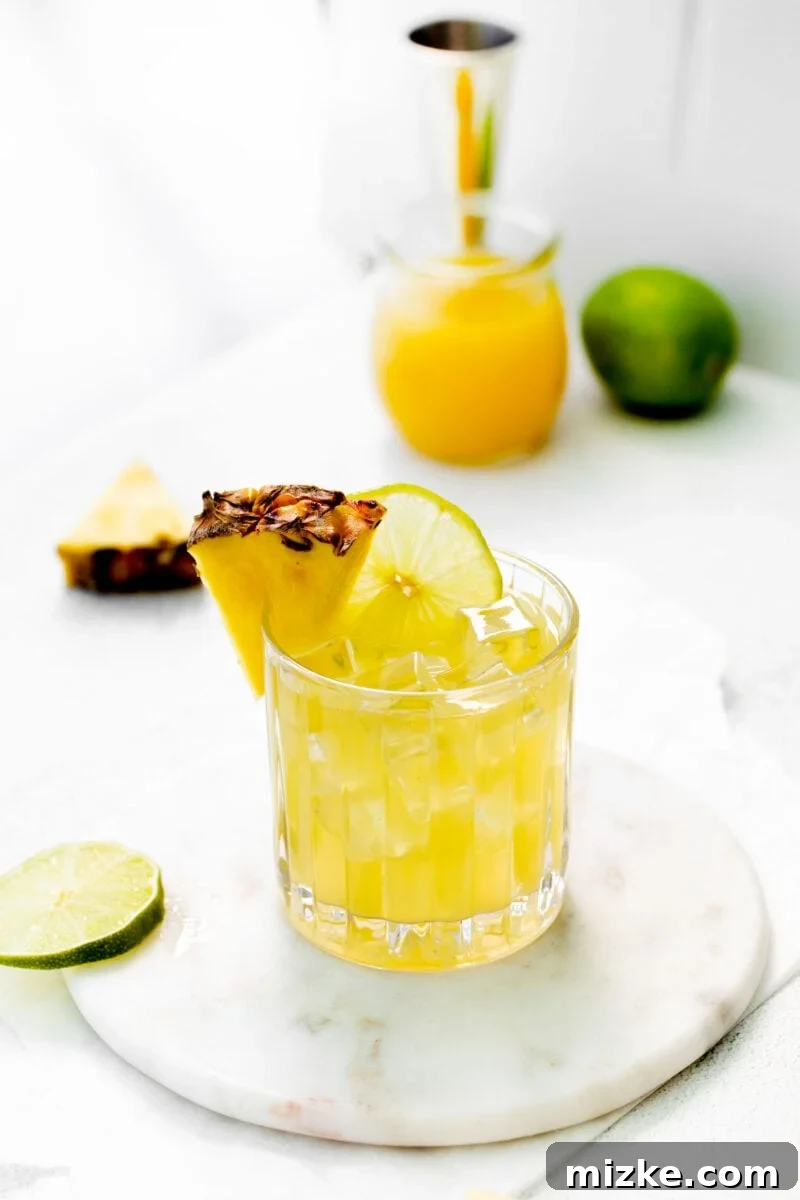 A beautifully presented glass of Pineapple Paloma, garnished with a vibrant pineapple wedge, sits on a surface, ready to be enjoyed.