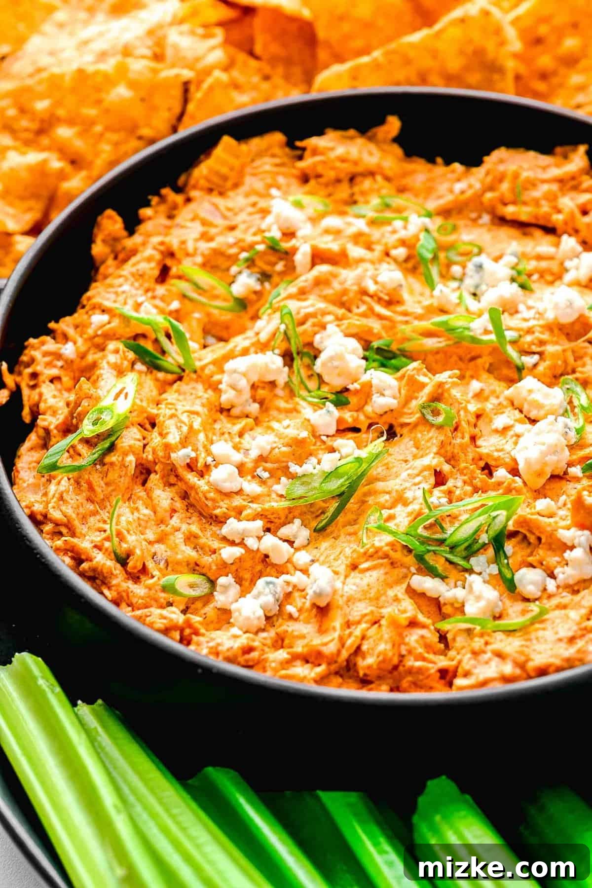 Crockpot buffalo chicken dip is the perfect party snack. It's creamy, loaded with chicken, and bursting with blue cheese and buffalo flavor. Closeup of creamy crockpot buffalo chicken dip in a rustic serving bowl, garnished with fresh herbs, alongside crisp celery sticks and golden tortilla chips.