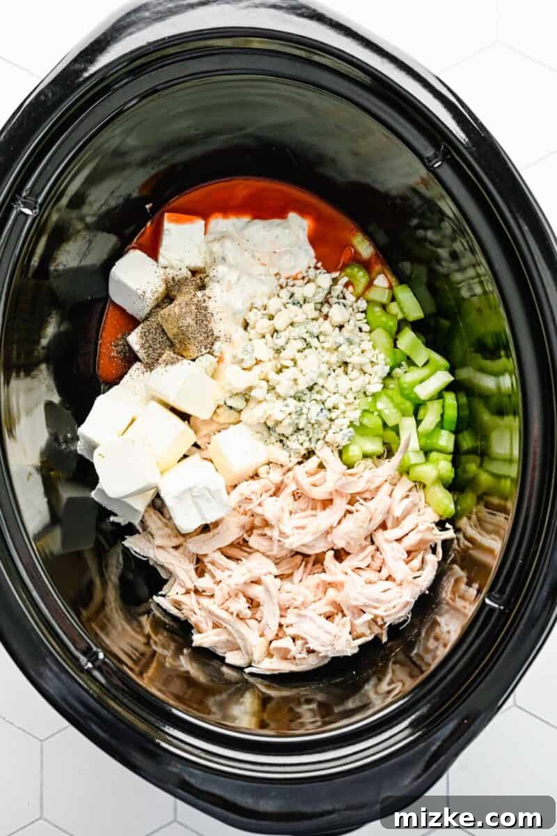 Crockpot buffalo chicken dip is the perfect party snack. It's creamy, loaded with chicken, and bursting with blue cheese and buffalo flavor. Adding all raw ingredients including shredded chicken, cubed cream cheese, hot sauce, celery, and blue cheese crumbles into the ceramic insert of a slow cooker.