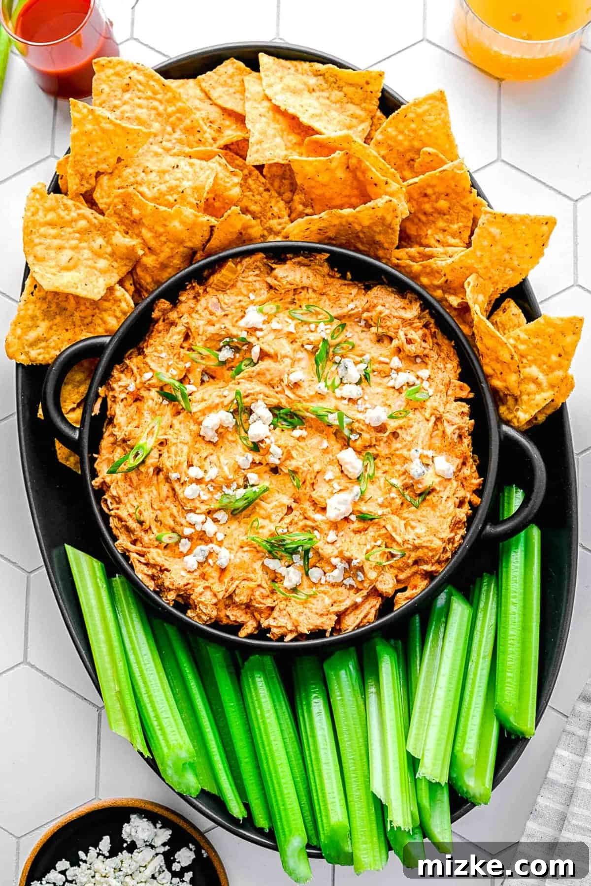 Crockpot buffalo chicken dip is the perfect party snack. It's creamy, loaded with chicken, and bursting with blue cheese and buffalo flavor. An inviting overhead shot of warm crockpot buffalo chicken dip presented in a beautiful serving bowl, surrounded by fresh celery sticks, carrot sticks, and an array of crispy tortilla chips.