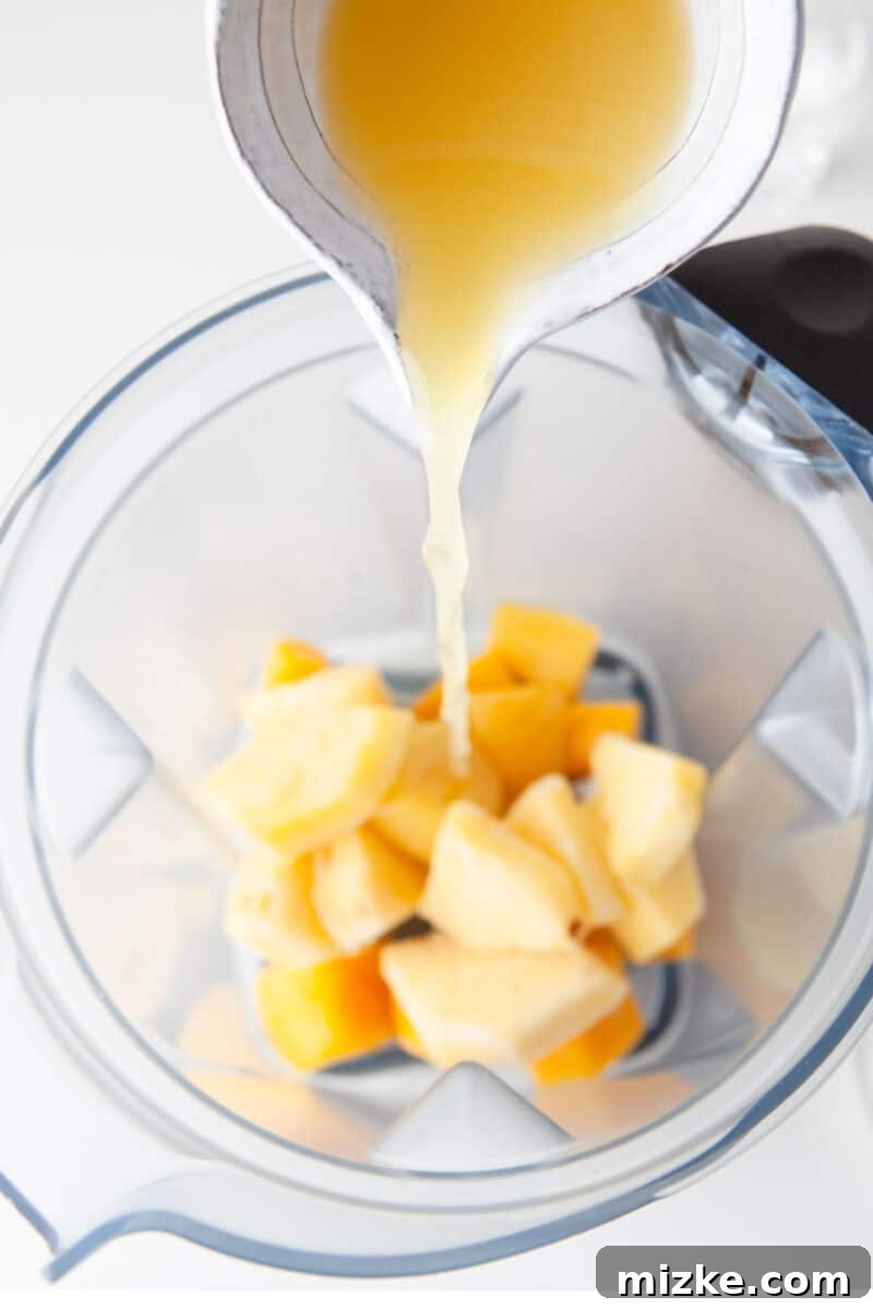Velvet Mango Sunset 4 Generous chunks of vibrant frozen mango are shown being added to a blender, ready to be transformed into a smooth cocktail.
