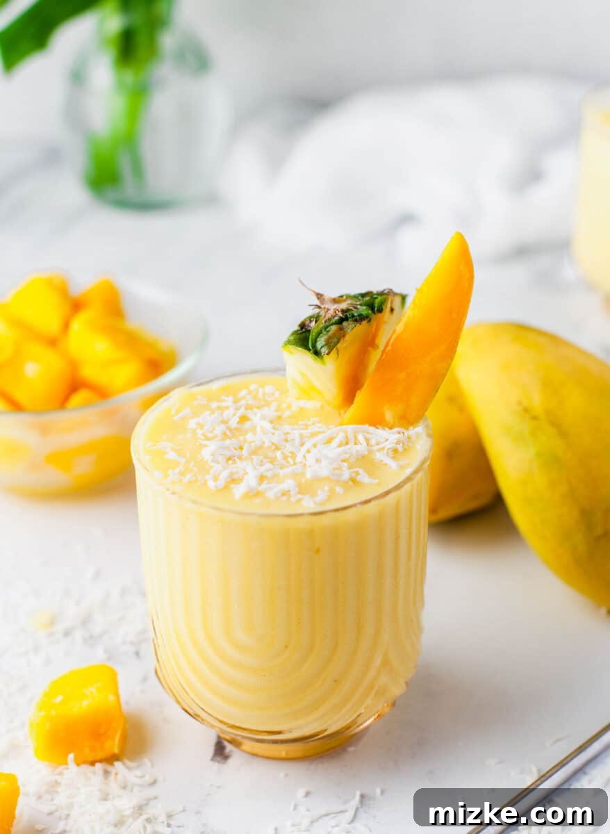 Velvet Mango Sunset 6 A pristine glass of Mango Colada, elegantly garnished with a fresh pineapple slice and a mango wedge, ready for sipping.
