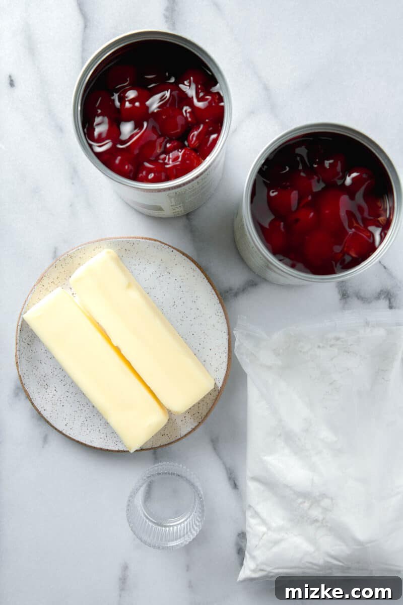 Effortless Cherry Delight 4 Ingredients laid out for cherry dump cake, including cans of cherry pie filling, a box of white cake mix, and sticks of butter.