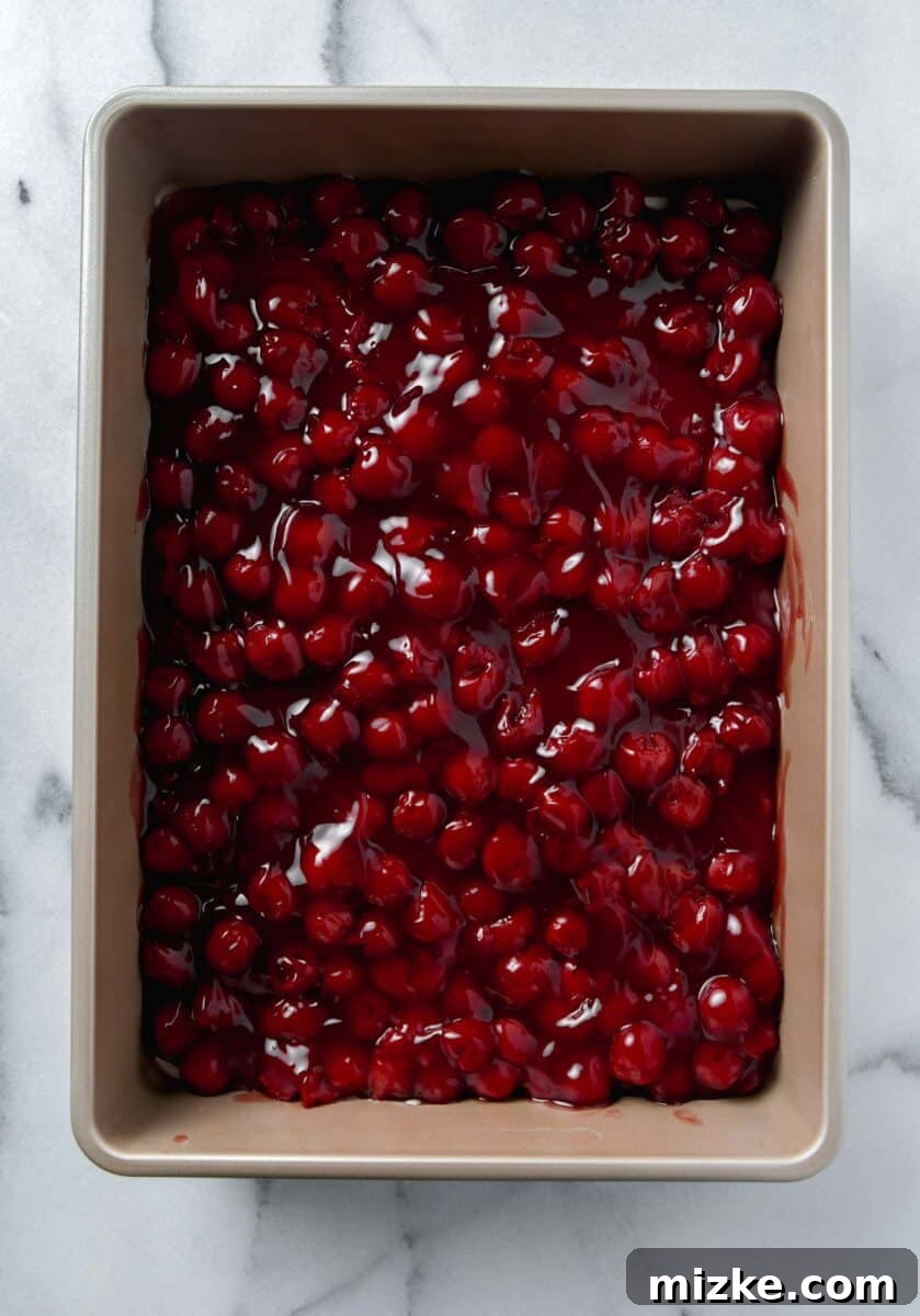 Effortless Cherry Delight 5 Cherry pie filling poured into a metal 9x13 baking dish, forming an even base layer.