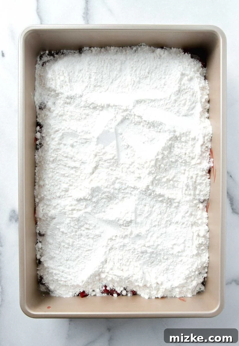 Effortless Cherry Delight 6 Dry white cake mix evenly spread over the cherry pie filling in a 9x13 baking pan, ready for butter.