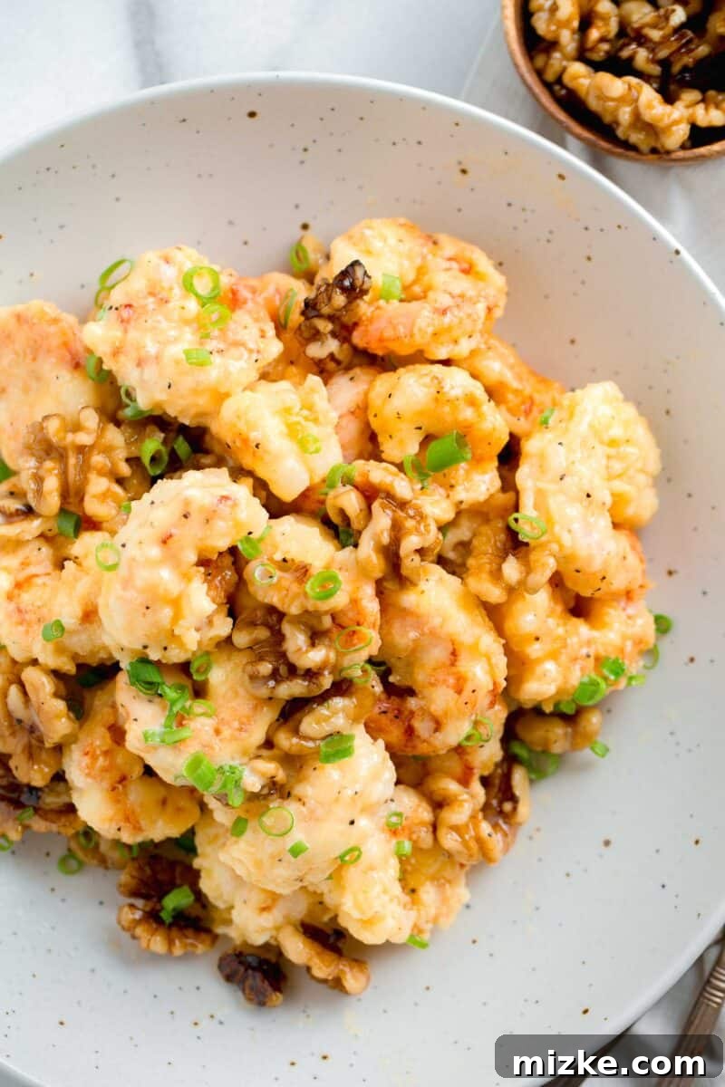 Crispy Honey Walnut Shrimp 2 Honey walnut shrimp in a speckled bowl next to a wooden bowl of walnuts, garnished with fresh scallions.