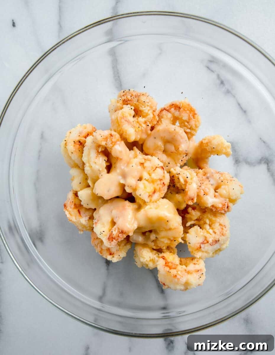 Crispy Honey Walnut Shrimp 12 The creamy honey sauce being poured over the fried shrimp in a clear glass bowl, ready for tossing.