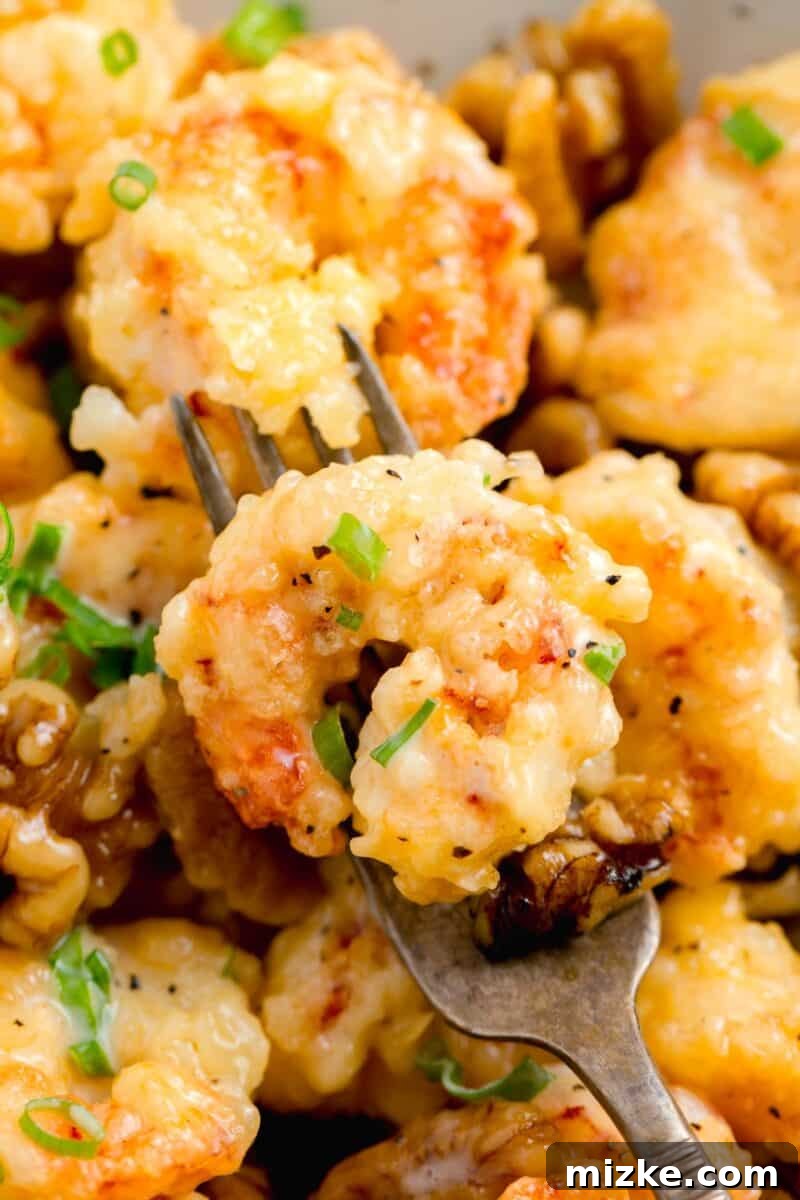 Crispy Honey Walnut Shrimp 14 An antique fork holds a honey walnut shrimp with fresh scallions, showcasing the crispy texture.