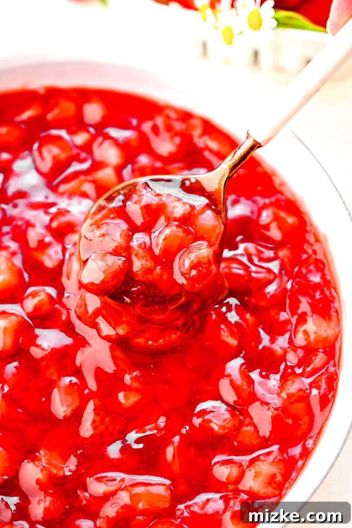 This vibrant strawberry cake filling is crafted from sweet strawberries, sugar, lemon juice, and cornstarch, cooked to a perfect, luscious thickness. Close-up of a spoon scooping a generous portion of thick strawberry cake filling from a glass bowl, showcasing its rich texture.