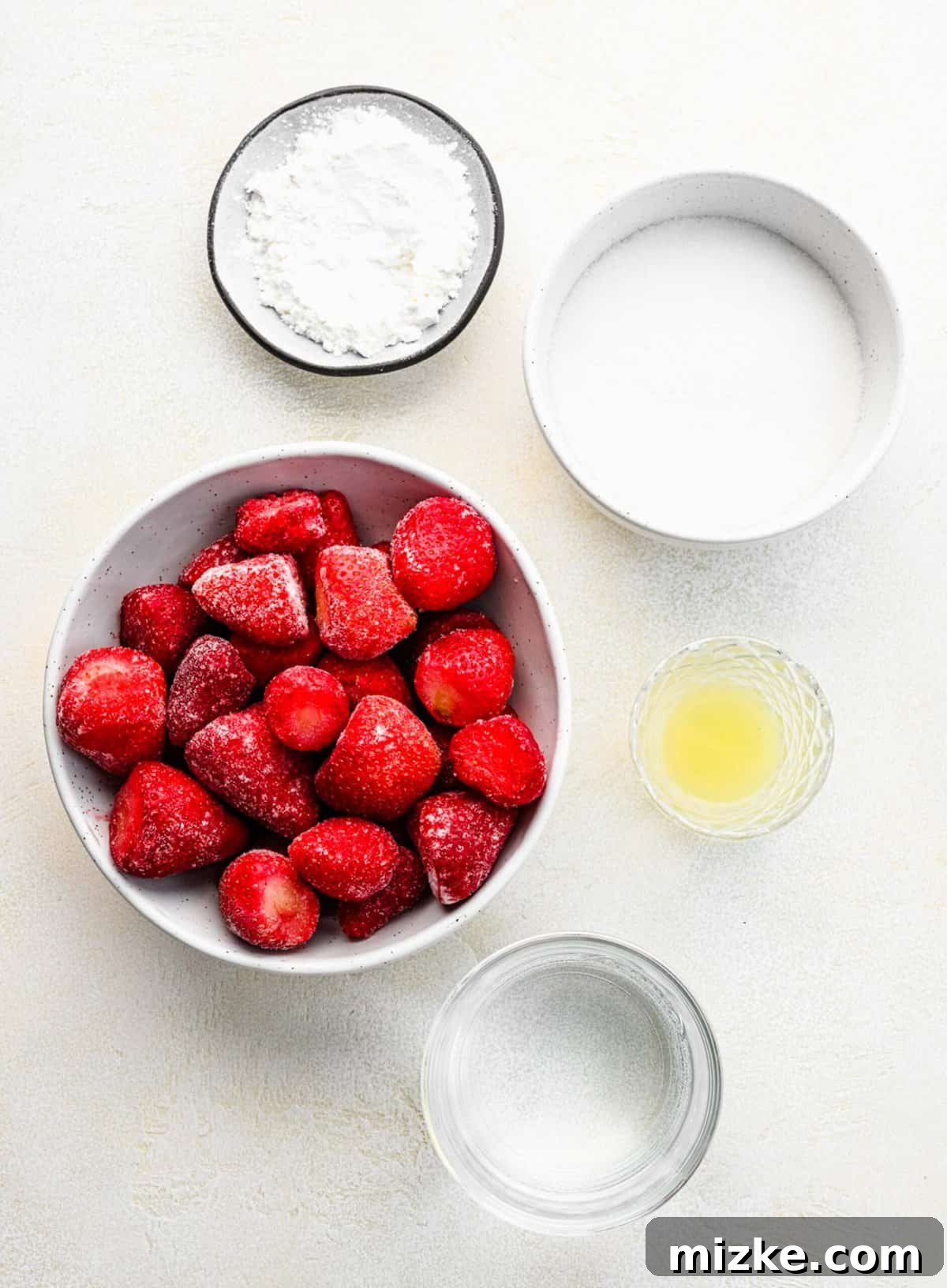 The essential ingredients for this sweet and tangy strawberry cake filling include diced strawberries, sugar, lemon juice, and cornstarch for thickening. Bowls neatly arranged with diced strawberries, granulated sugar, cornstarch, and lemon juice, showcasing the simple ingredients for the cake filling.