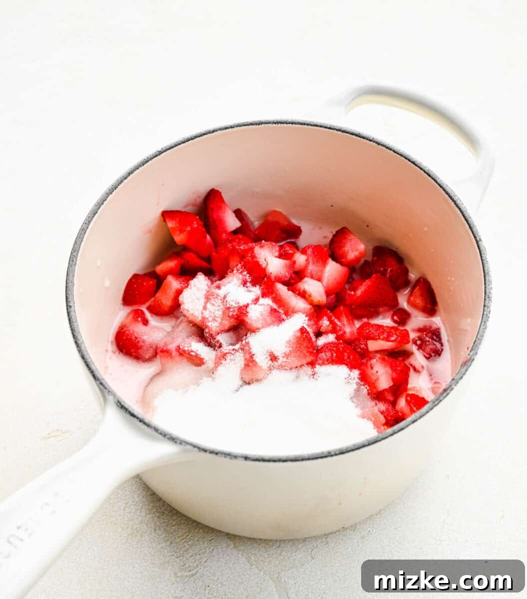 Combining all ingredients: strawberries, sugar, and lemon juice join the cornstarch mixture in the pot, starting the cooking process for the cake filling. Diced strawberries, sugar, and lemon juice being added to the cornstarch slurry in a pot, ready for cooking.
