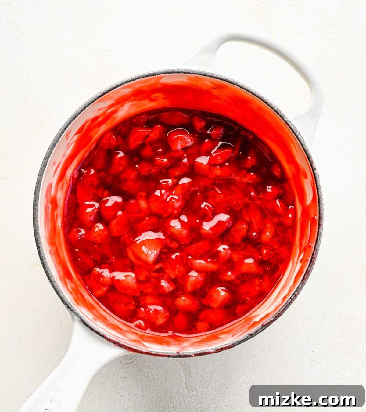 Homemade strawberry cake filling simmering on the stove, transforming into a thick, luscious dessert component. Cooking strawberry cake filling in a pot on the stovetop, showing the fruit beginning to break down and thicken.