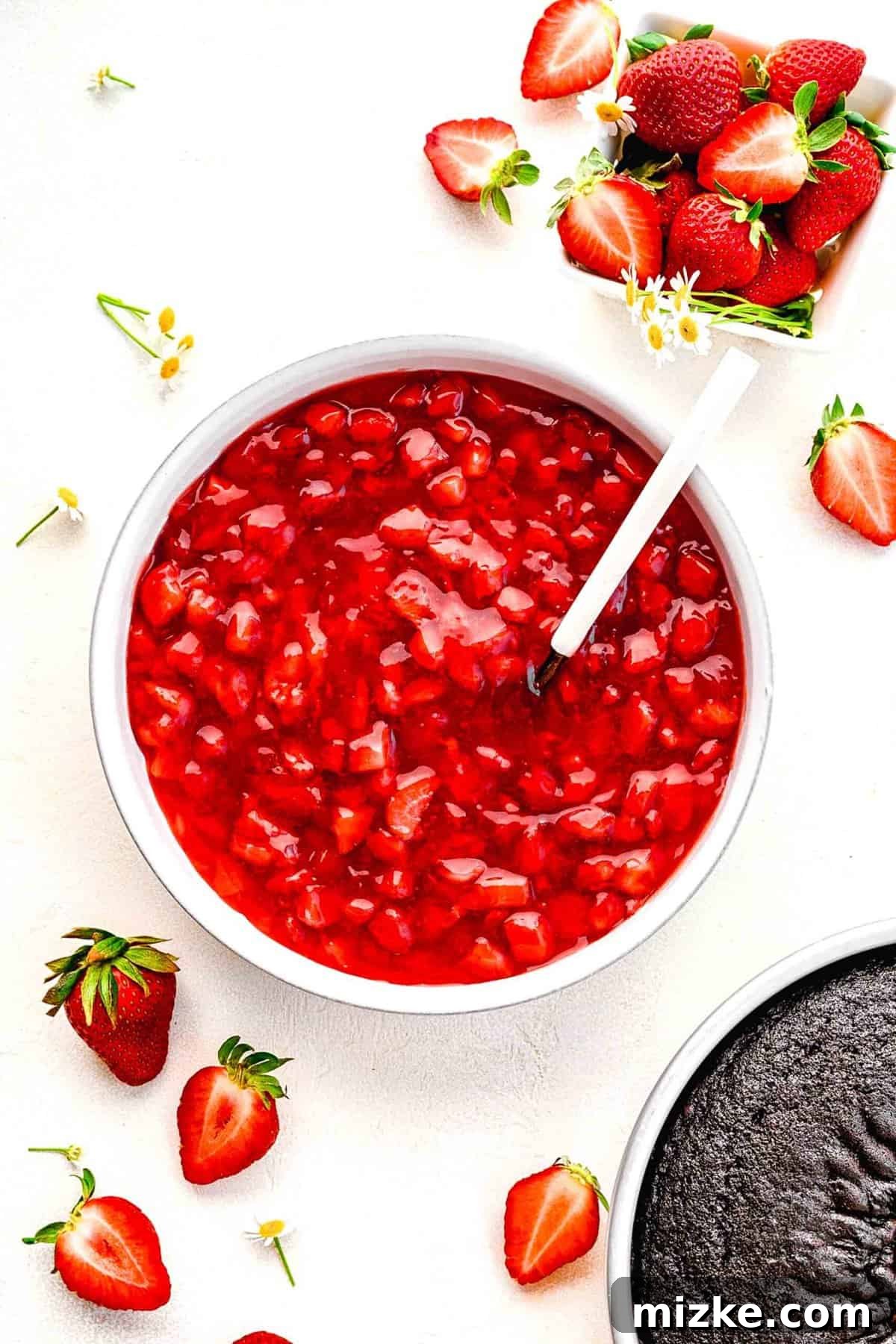 A beautifully arranged overhead view of the finished strawberry cake filling in a bowl, perfect for various dessert applications. Overhead shot of a bowl of glossy strawberry cake filling, garnished with fresh whole strawberries, highlighting its vibrant color and smooth texture.