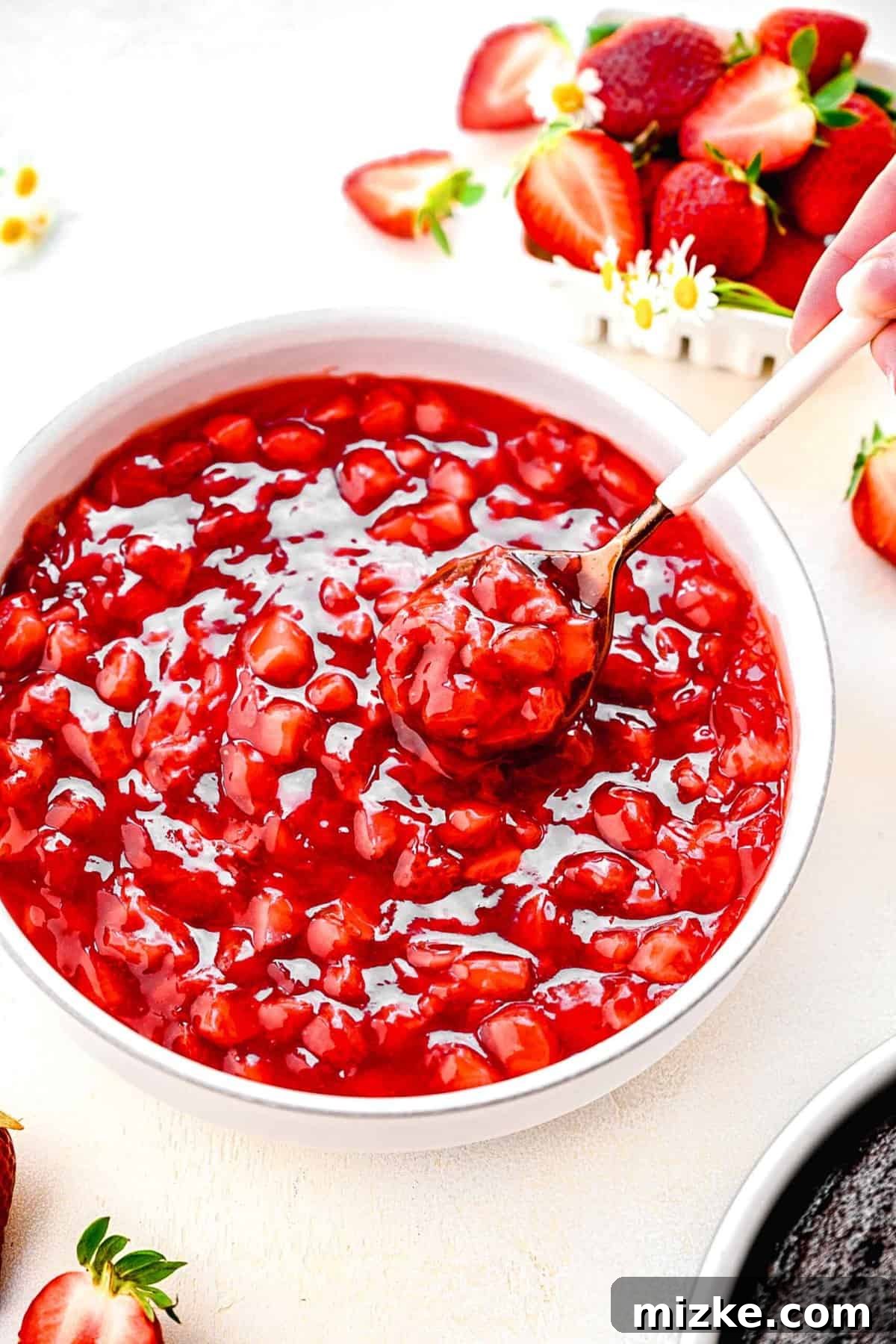 Enjoying a taste of the delicious strawberry cake filling, perfect for any sweet creation. A close-up of a spoonful of strawberry cake filling being lifted from a bowl, with fresh strawberries scattered nearby.