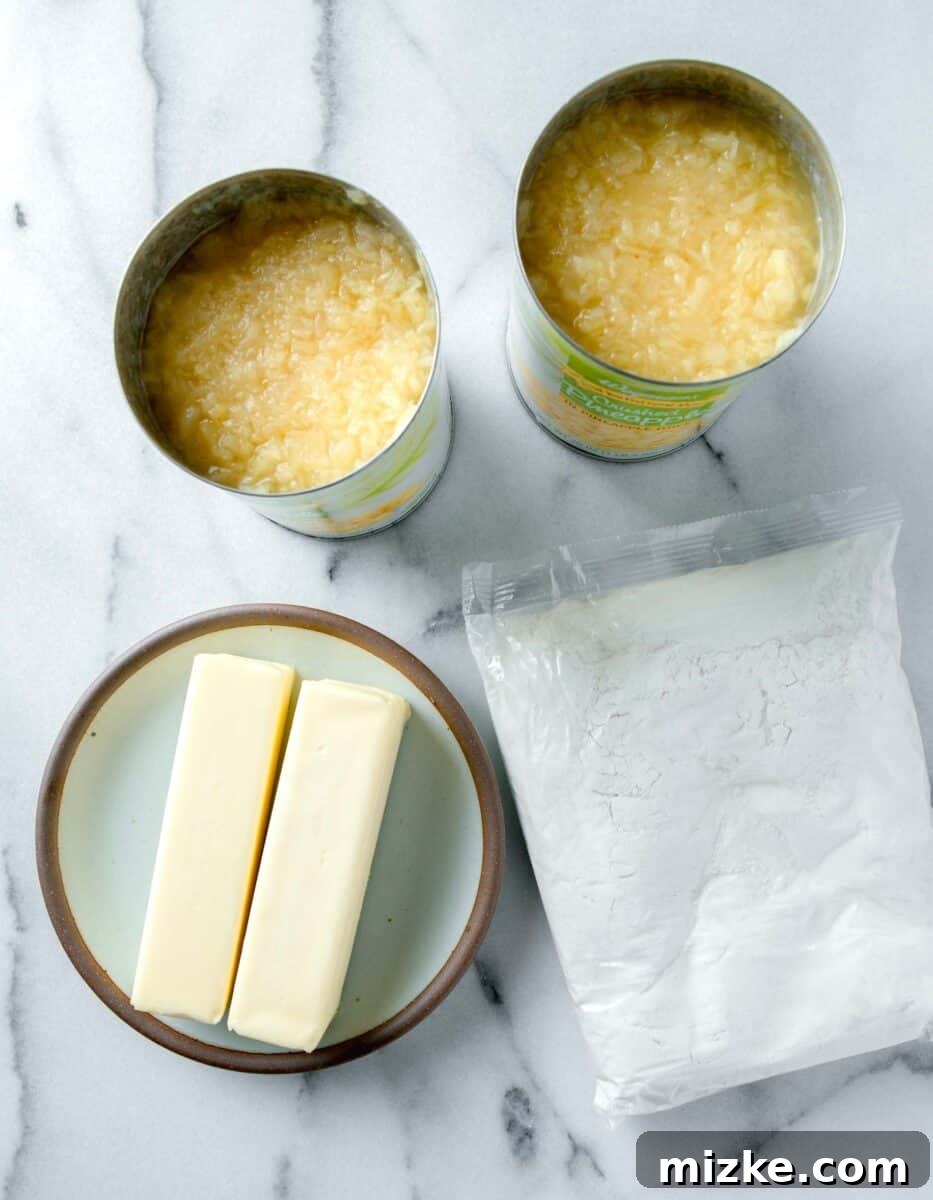 The simple ingredients laid out for making pineapple dump cake: canned crushed pineapple, a box of white cake mix, and sticks of butter.