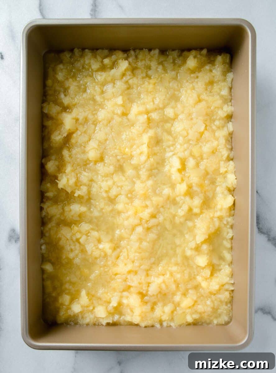 Crushed pineapple evenly spread in the bottom of a 9x13 inch gold baking dish, ready for the next layer.