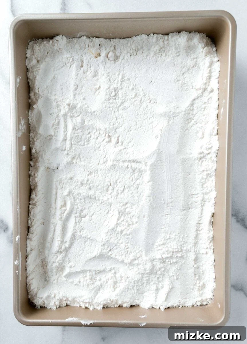 White boxed cake mix sprinkled in an even layer over the crushed pineapple in a 9x13 inch gold baking dish.