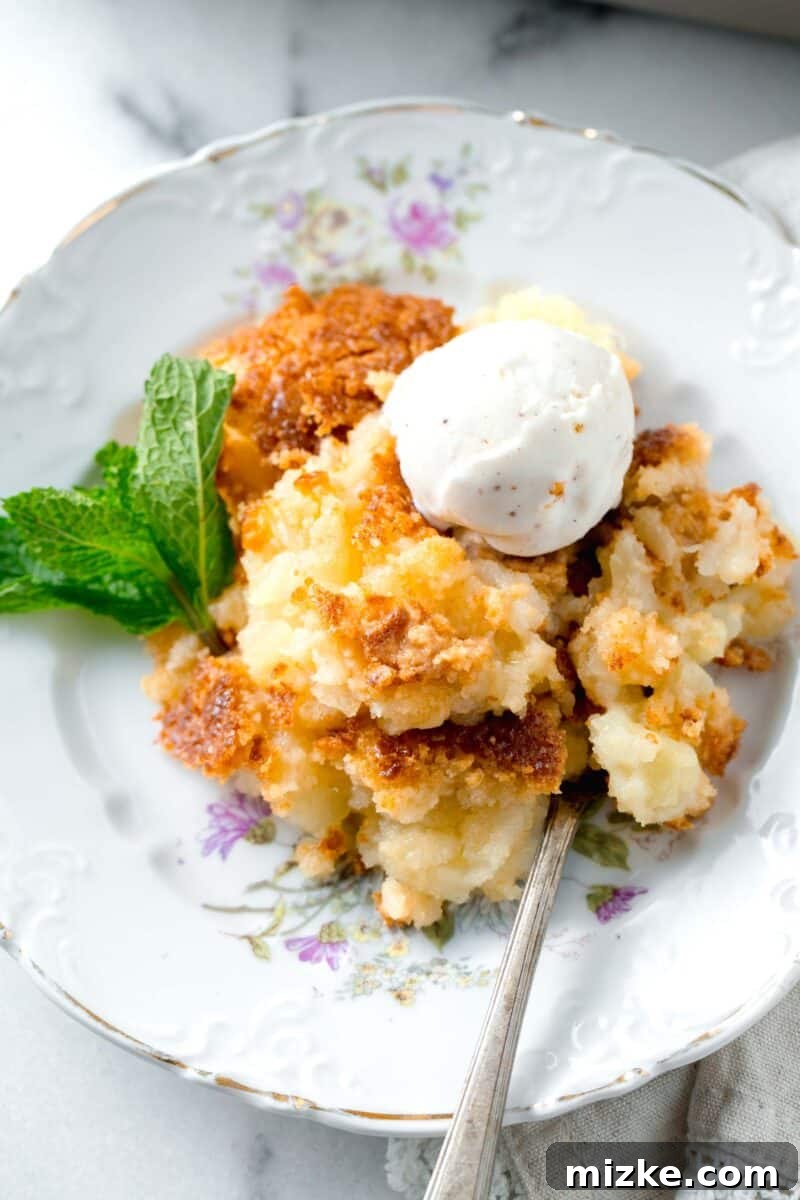 A tempting slice of pineapple dump cake on a beautifully decorated dessert plate, garnished with a sprig of mint and a melting scoop of vanilla ice cream.