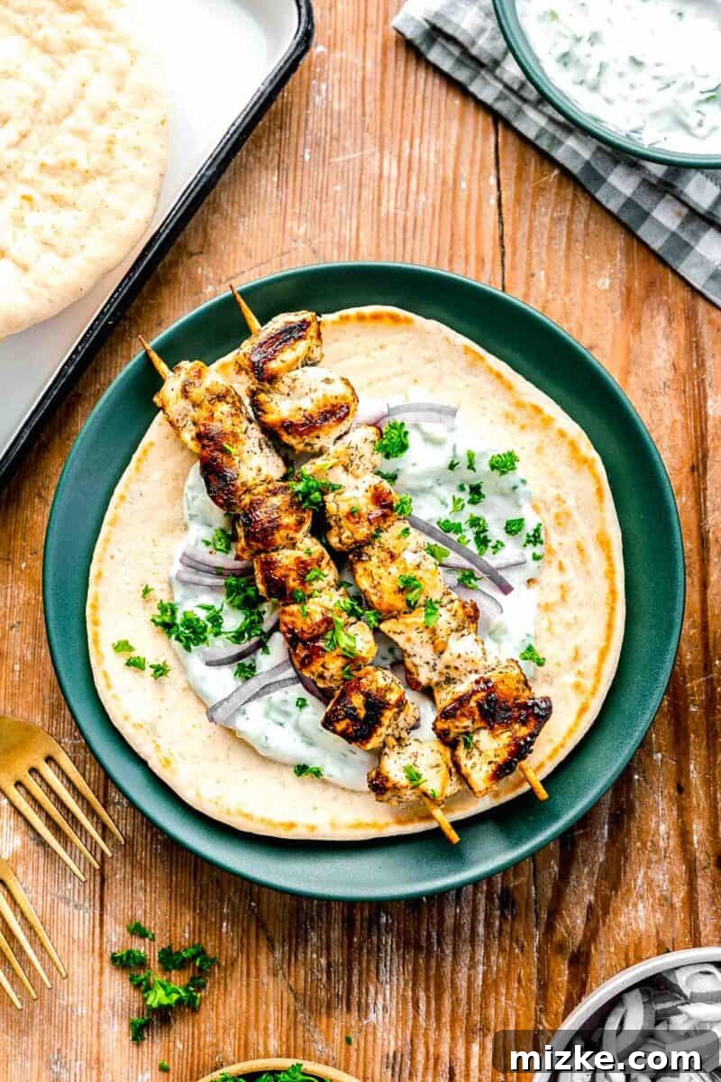 Greek chicken souvlaki skewers on top of pita with tzatziki sauce and fresh parsley on a green plate