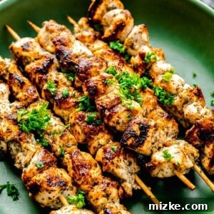 Greek chicken souvlaki skewers on a green plate with fresh parsley on top