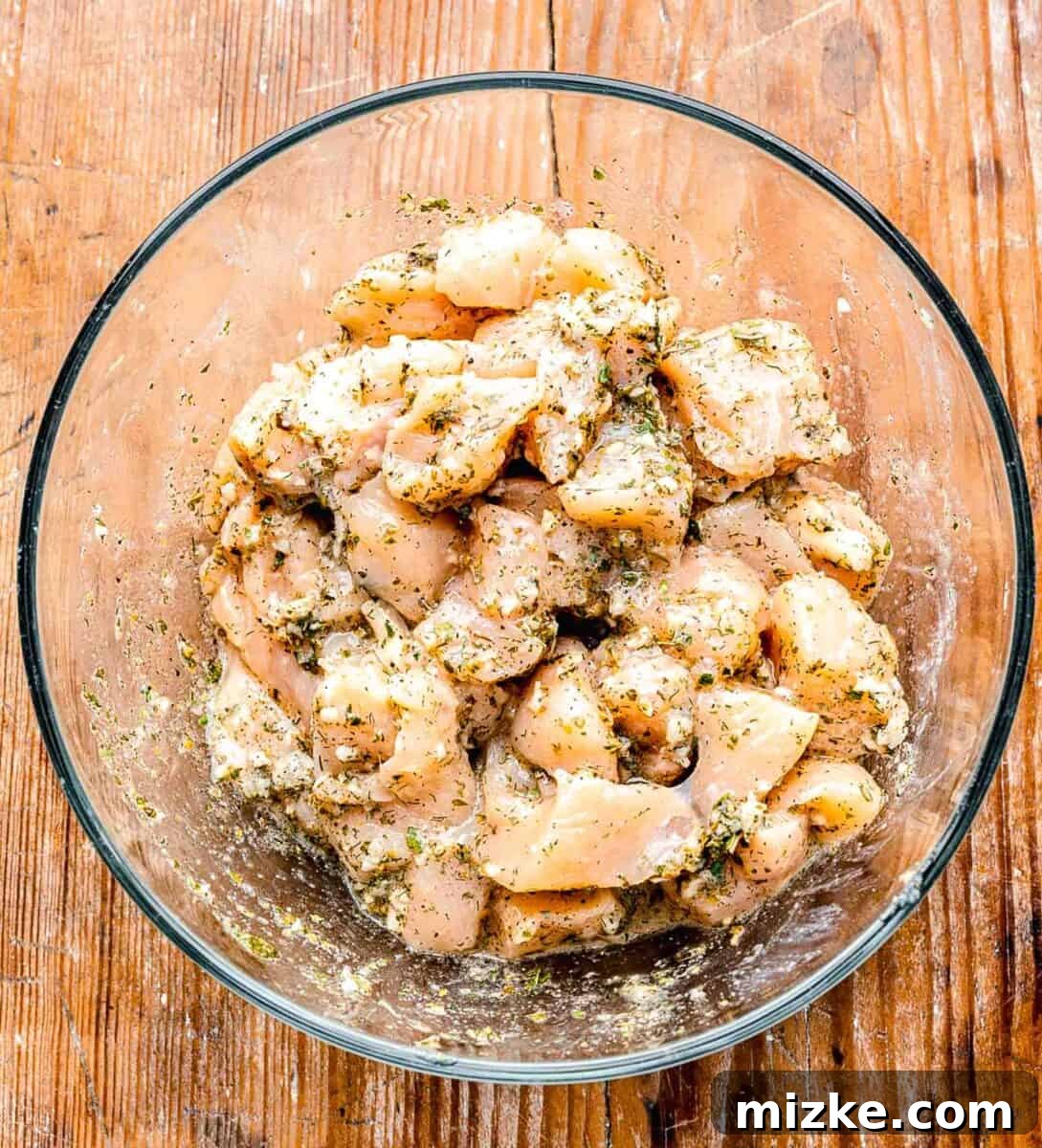 Raw chicken cubes tossed in Greek seasoning in a clear bowl