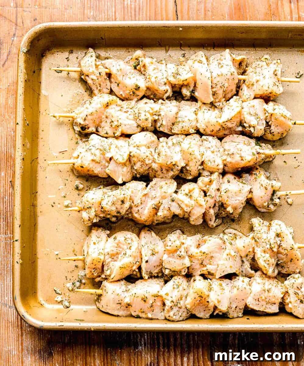 Marinated chicken skewered on wooden skewers on a rimmed baking sheet