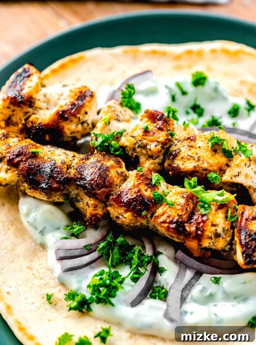 Greek chicken souvlaki skewers on top of pita and tzatziki sauce