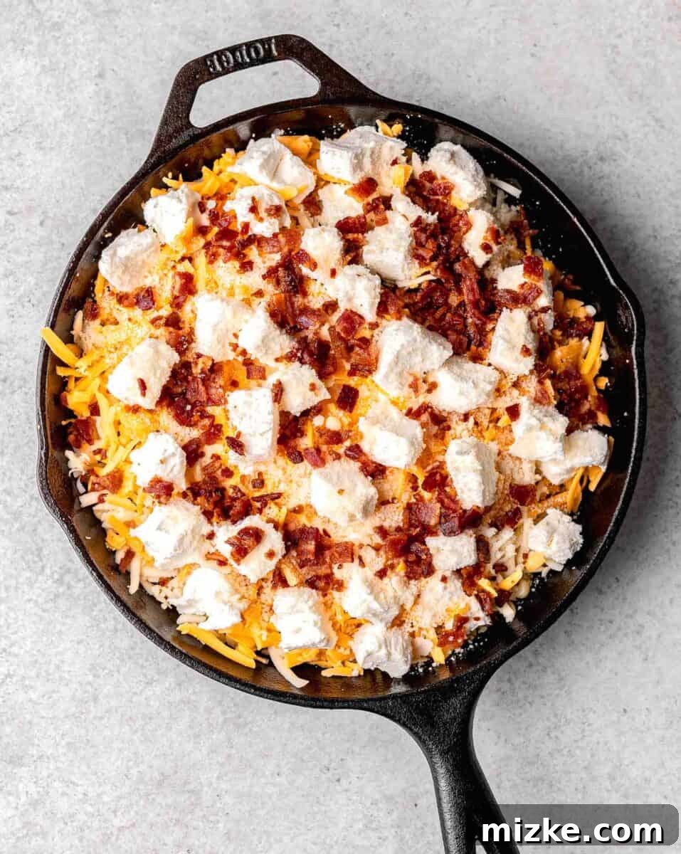 all the ingredients for corn dip in a cast iron skillet. cubes of cream cheese and bacon bits can be seen on top
