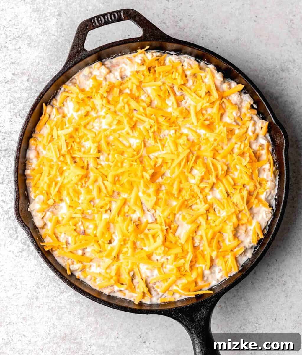 extra shredded cheddar cheese sprinkled on top of the corn dip mixture in the cast iron skillet