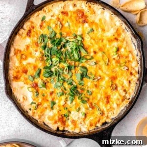 freshly baked corn dip in a cast iron skillet with fresh cilantro and green onions sprinkled on top next to tortilla chips and beer