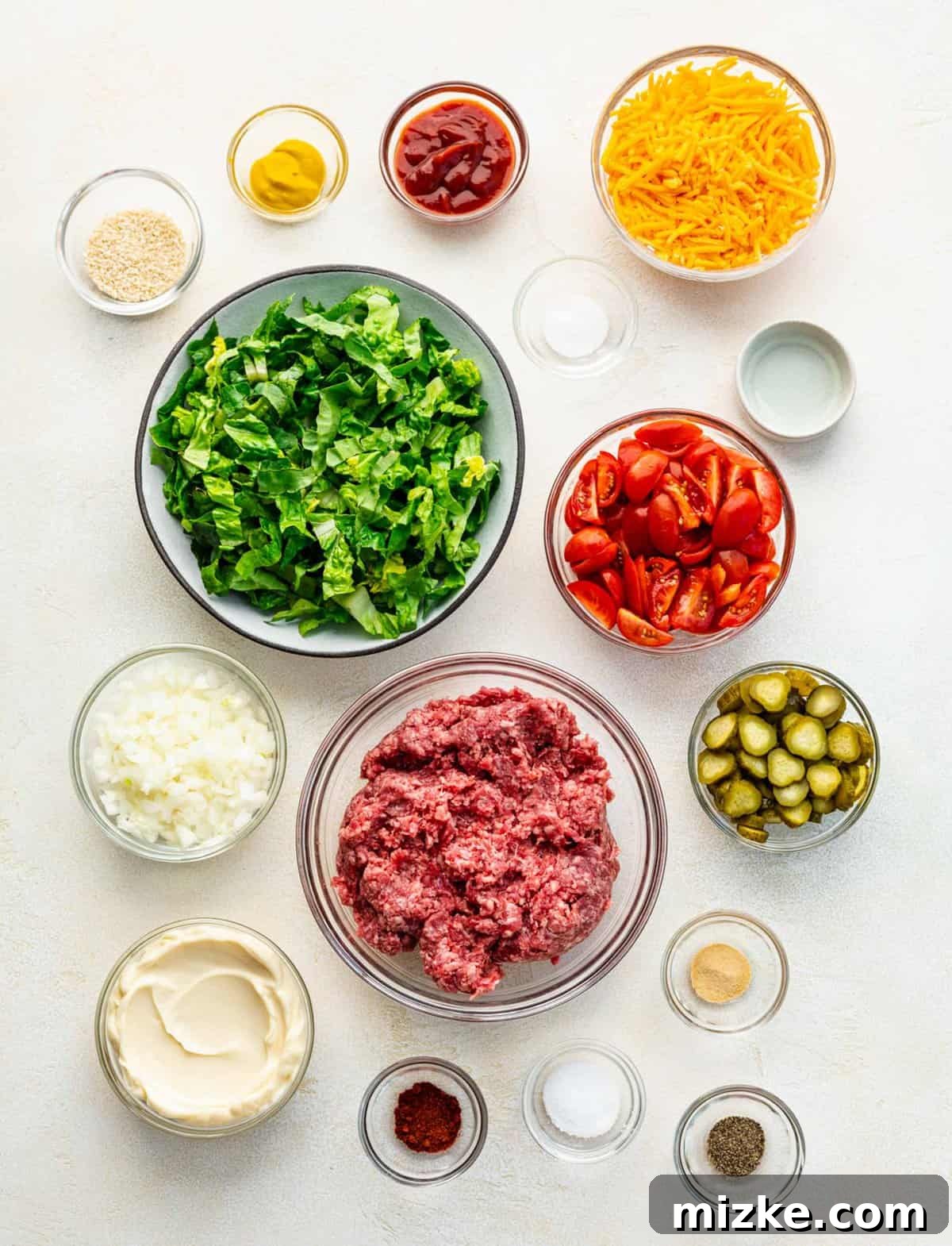 Big Mac salad is made up of cooked ground beef tossed together with crispy lettuce and tomatoes in a creamy, thousand islands-esque dressing. Ingredients for Big Mac salad separated into bowls.
