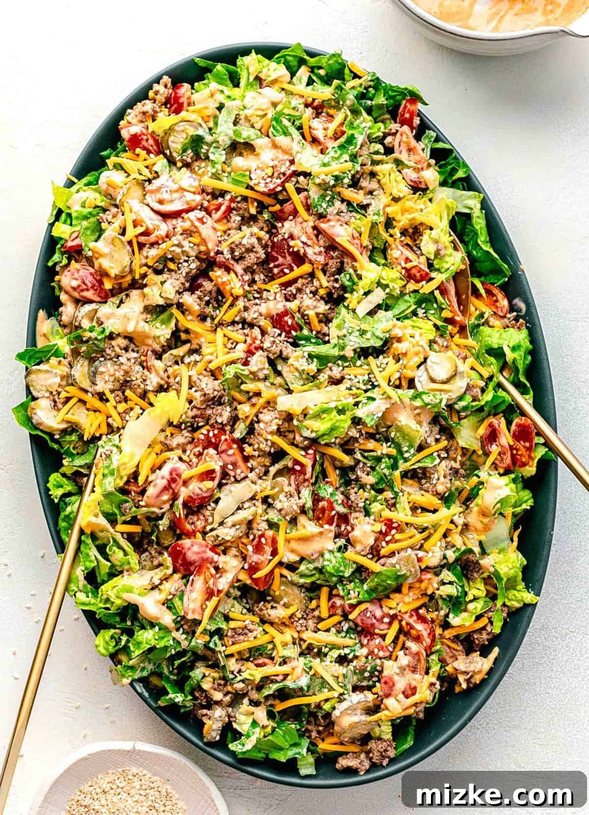 Big Mac salad is made up of cooked ground beef tossed together with crispy lettuce and tomatoes in a creamy, thousand islands-esque dressing. Big Mac salad tossed together on a serving platter with serving tongs.