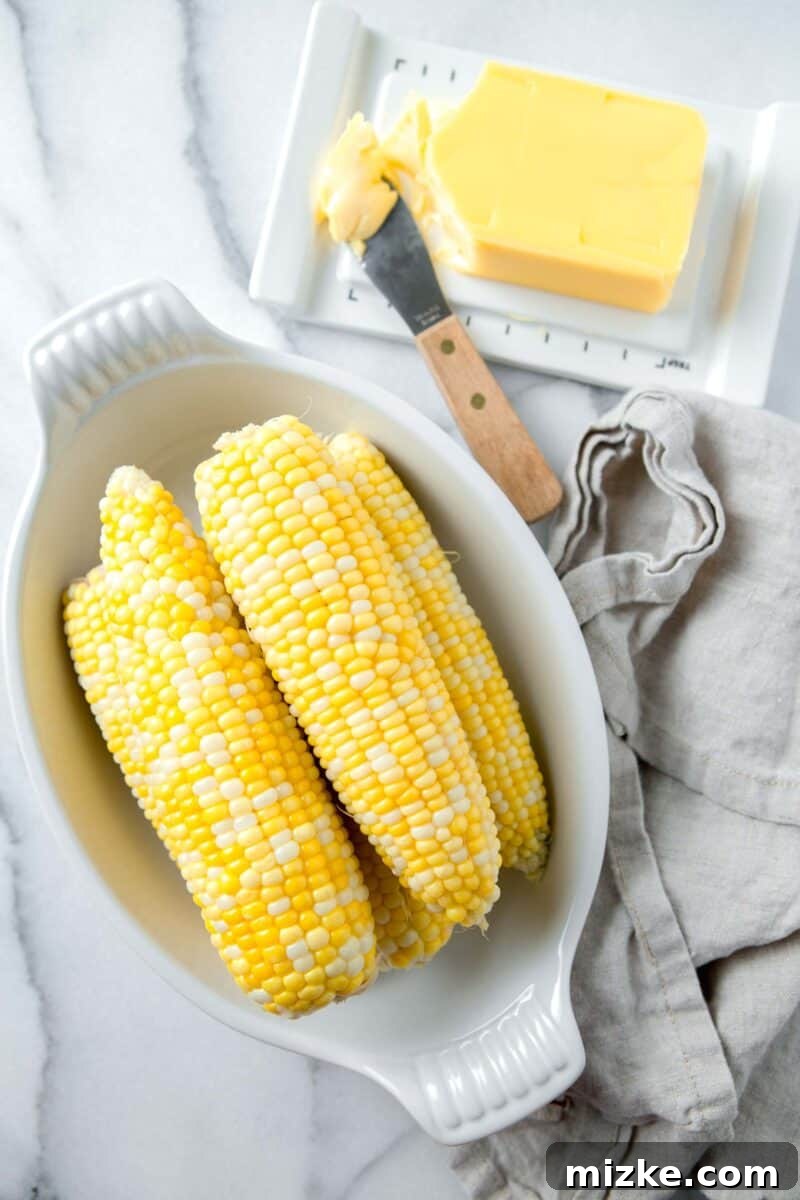 Instant Pot Corn Perfection 2 cooked corn on the cob in a casserole dish next to a linen towel and butter