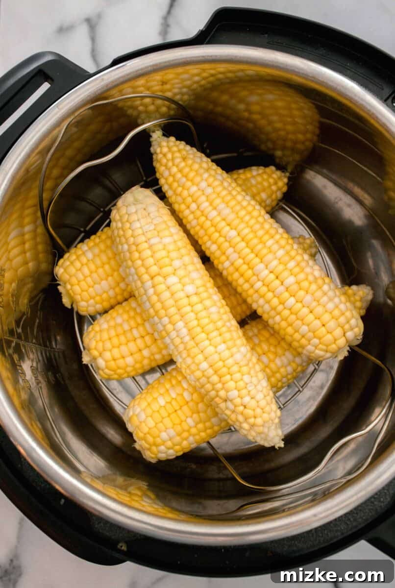 Instant Pot Corn Perfection 4 shucked corn stacked on a metal trivet on the inside of an instant pot/pressure cooker