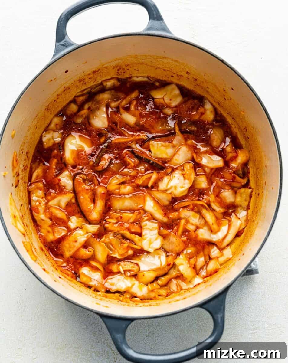 Building the Broth: Adding Key Flavorings to Kimchi Ramen Base Adding gochujang paste, kimchi juice, and soy sauce to the sautéed mushroom, kimchi, and garlic mixture in a soup pot.