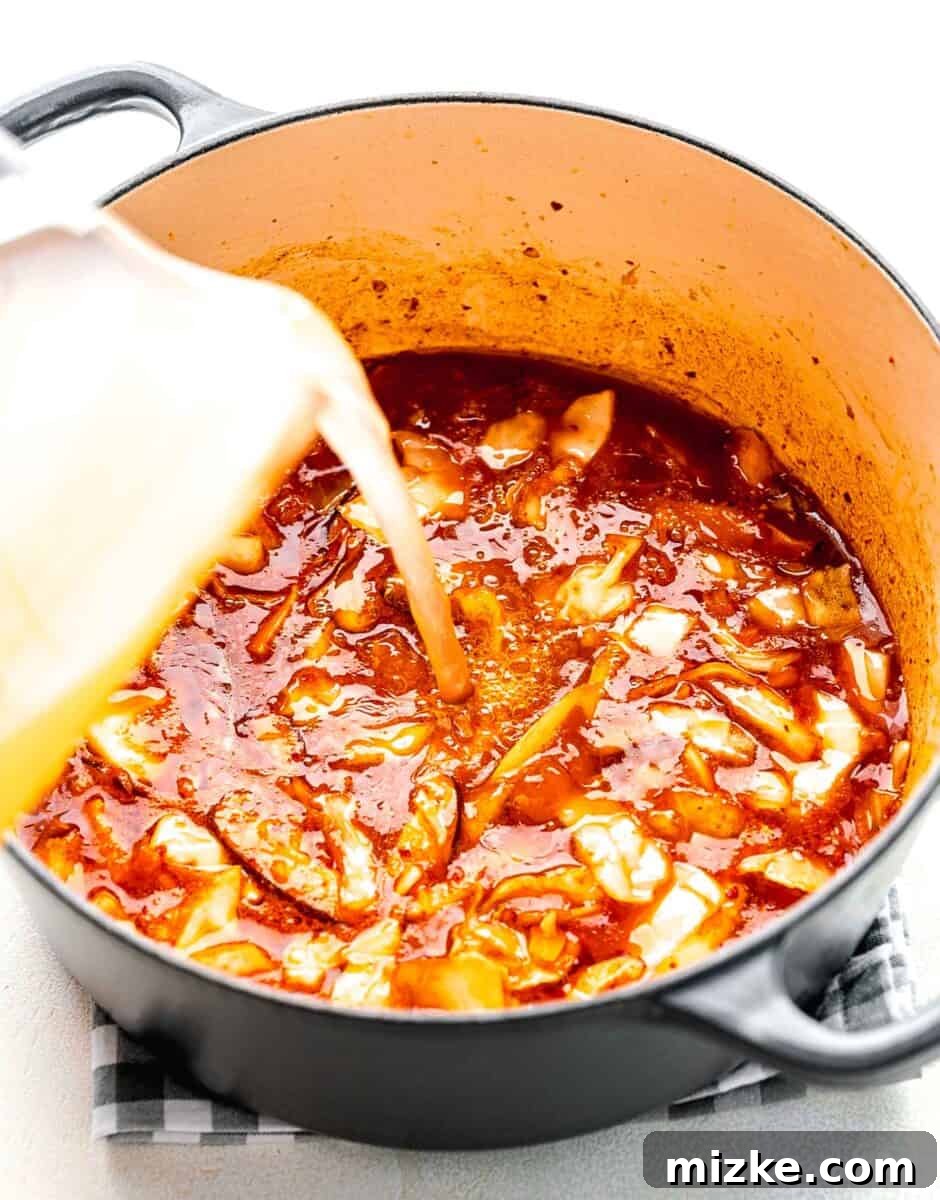 Completing the Broth: Adding Chicken Stock for Kimchi Ramen Pouring chicken broth into the soup pot containing the flavorful mixture of gochujang, kimchi juice, soy sauce, sautéed mushrooms, kimchi, and garlic.